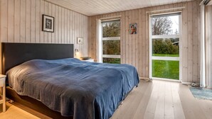 Een slaapkamer met een groot bed, houten wanden en uitzicht op het landschap.