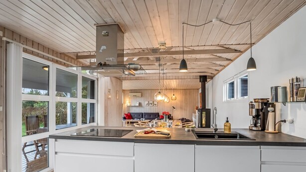 Een moderne keuken met een groot schiereiland, een houten plafond en grote ramen.