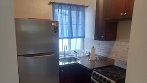 A compact kitchen with a refrigerator, sink, stove, and wooden cabinets. - Studio Apt on 7 Mile Beach at Negril Beach Club (Negril)