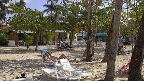A beach with white lounge chairs, palm trees, and a building in the background. - Studio Apt on 7 Mile Beach at Negril Beach Club (Negril)