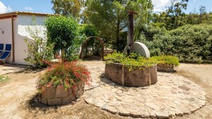 A rustic outdoor area with stone planters, a wooden archway, and a white building with a blue chair.
