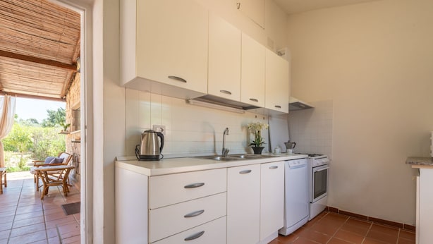 Une cuisine moderne avec des armoires blanches, un four encastré et un lave-vaisselle. Un coin repas avec une table et des chaises se trouve à l’extérieur.