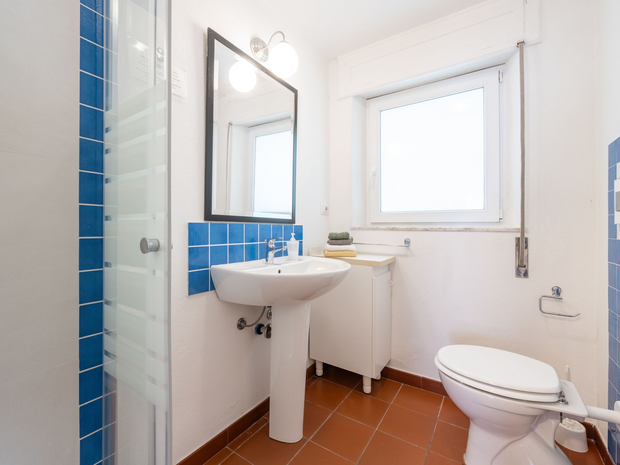 A bathroom with a white sink, a mirror, a toilet, and a window.