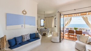A spacious living area with a white sofa, a dining table with chairs, and a view of the sea through large glass doors. - Villa Grete by Interhome (Pula)