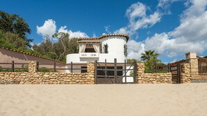 A white building with a stone wall and gate, surrounded by a sandy area and greenery. - Villa Grete by Interhome (Pula)