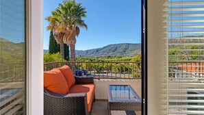A balcony with a wicker sofa and a glass table, overlooking a vineyard and mountains. - Mediterranean House in De Luz (Temecula)