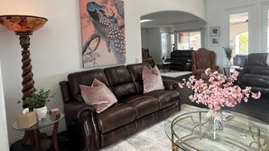 A living room with a brown leather sofa, a glass coffee table, and a painting of birds on the wall. - Mediterranean House in De Luz (Temecula)