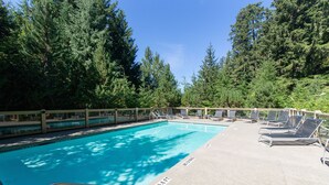 Ein Swimmingpool mit Liegestühlen und einer Holzterrasse, umgeben von Bäumen.