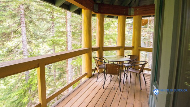 Eine Holzterrasse mit Tisch und Stühlen, mit Blick auf ein bewaldetes Gebiet.