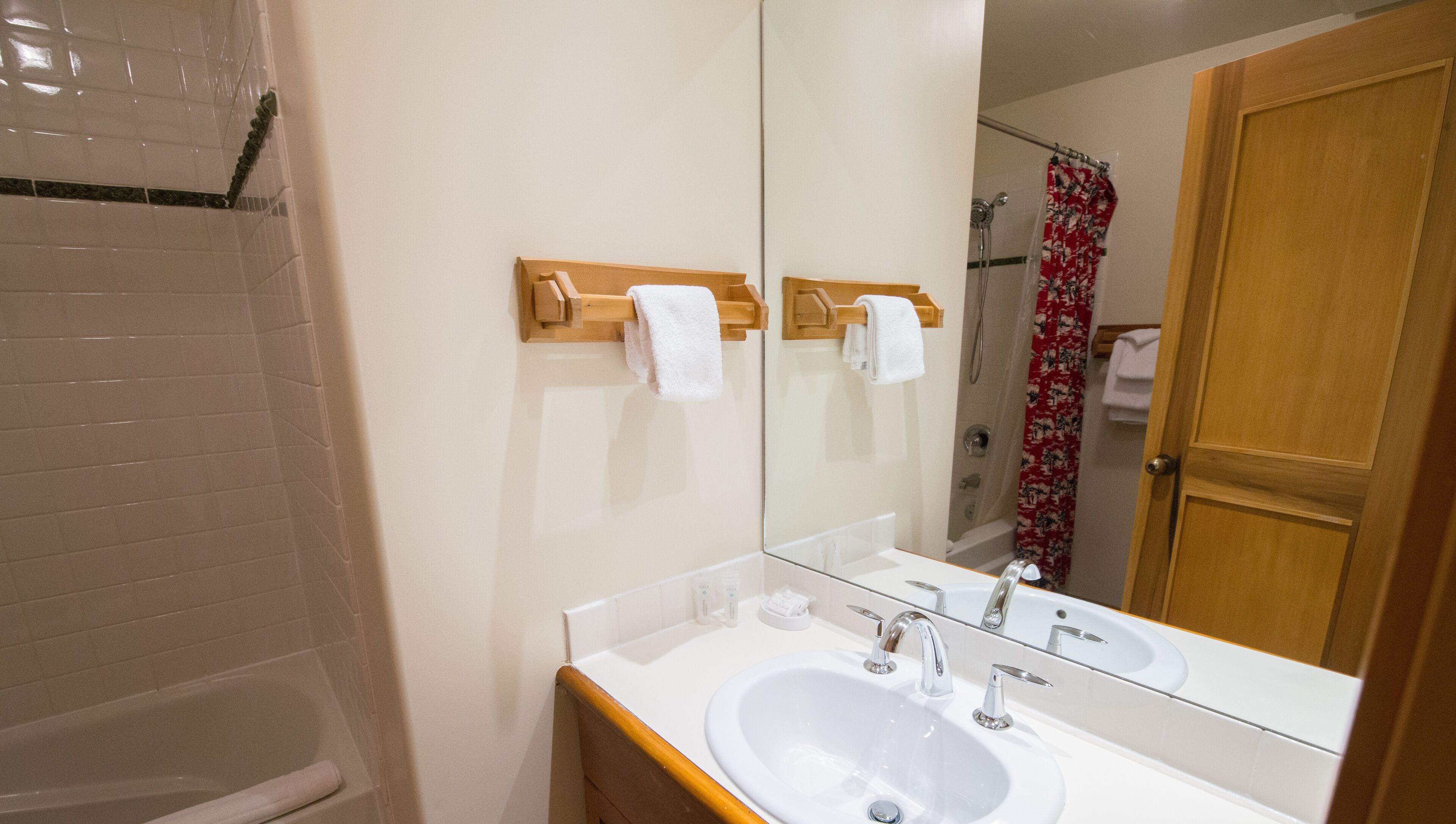 A bathroom with a white sink, two mirrors, a wooden towel rack, and a shower with a floral curtain.
