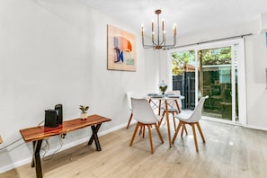 A dining area with a wooden table, white chairs, a chandelier, and a sliding glass door leading to a garden. - Modern Designer Oasis 208 (Irving)