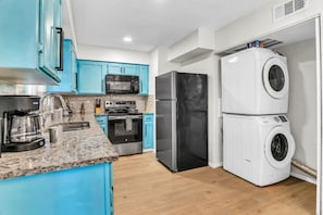 A modern kitchen with blue cabinets, a stainless steel refrigerator, a microwave, a coffee maker, and a stacked washer and dryer.