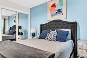A bedroom with a large bed, a nightstand, a bedside table, and a mirror. - Modern Designer Oasis 208 (Irving)