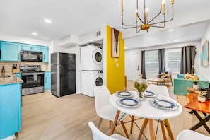 A modern kitchen with a microwave, oven, and refrigerator, a dining area with a table set for two, and a yellow accent wall.
