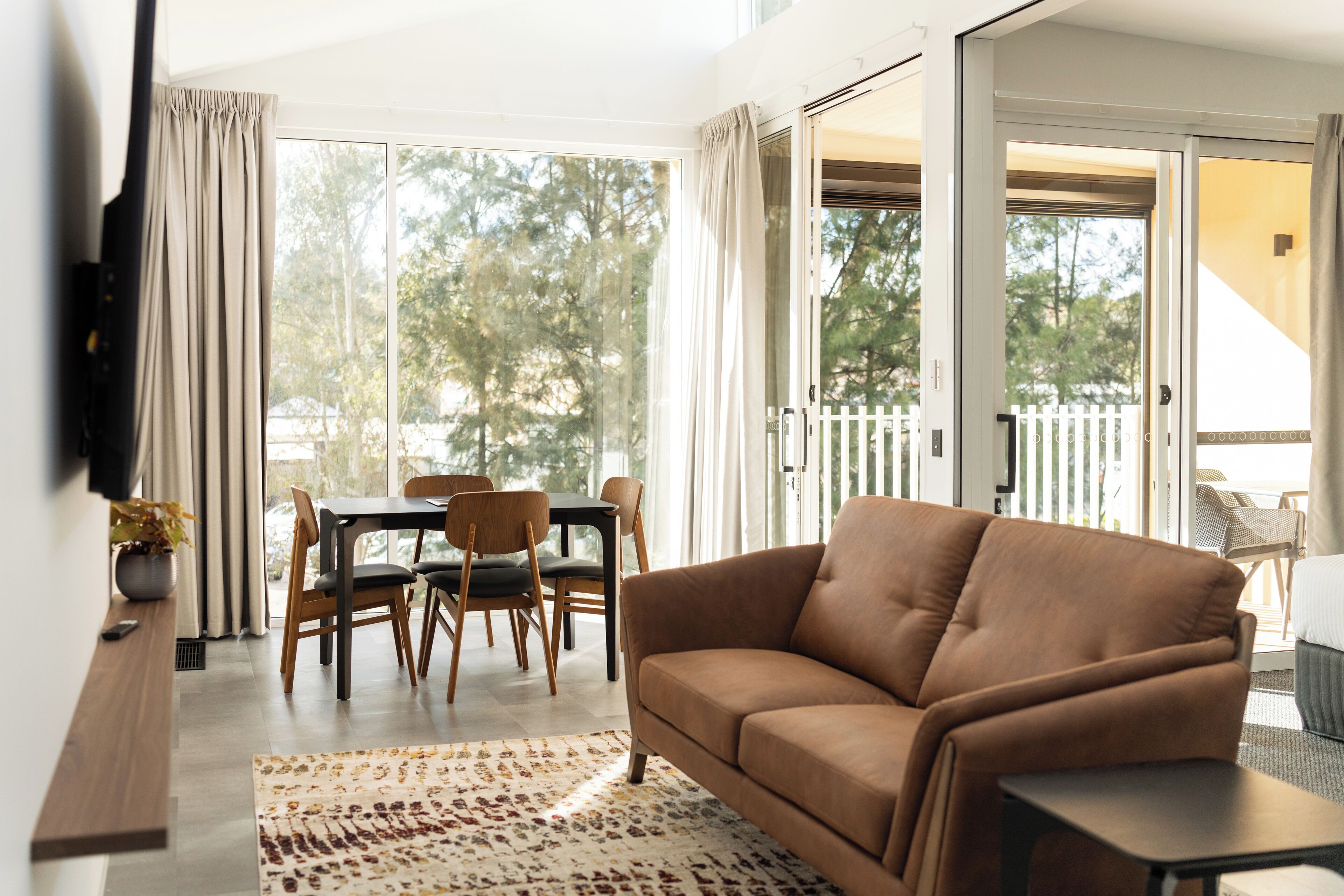 A modern living room with a sofa, a dining table with chairs, and a large sliding glass door leading to an outdoor area.