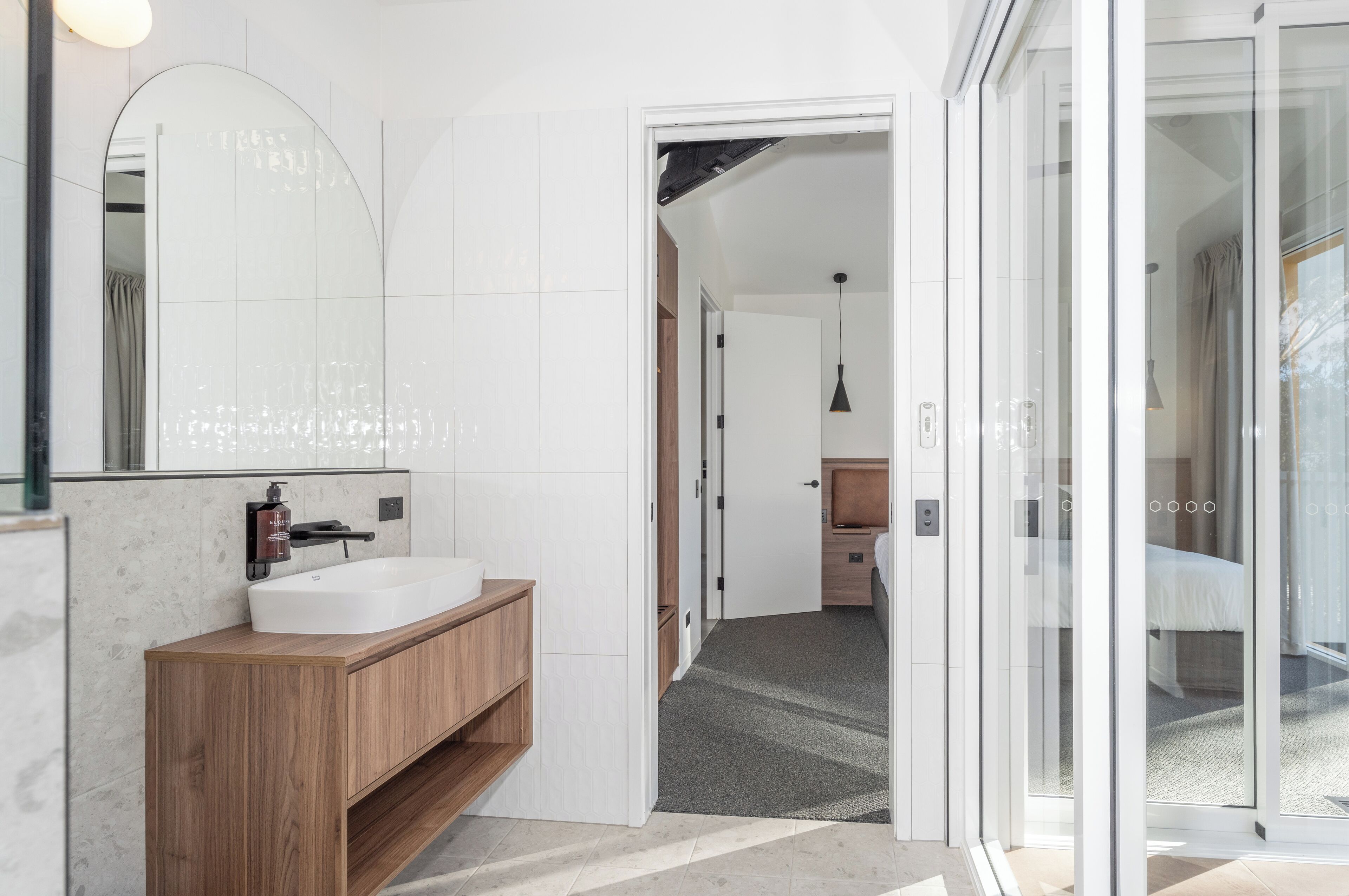 Een moderne badkamer met een grote spiegel, een houten wastafelmeubel en een witte wastafel.