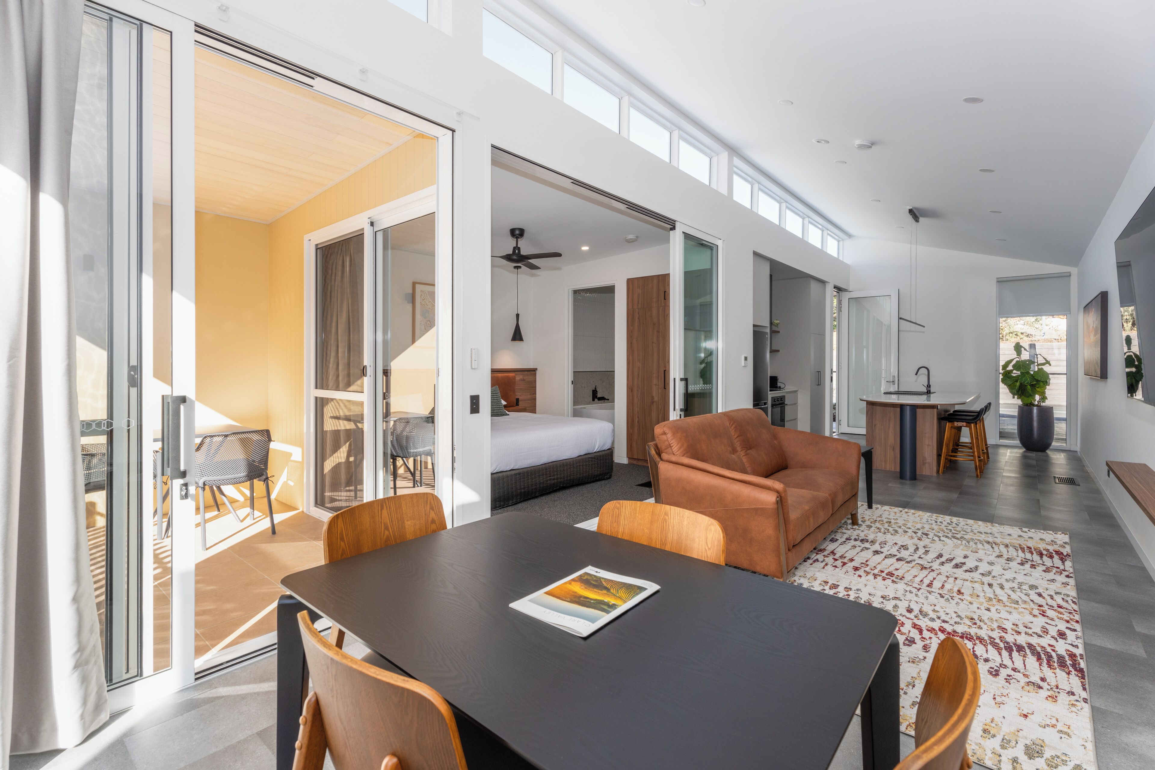 A modern, open-plan living space with a dining area, a sofa, a bed, and a kitchen.