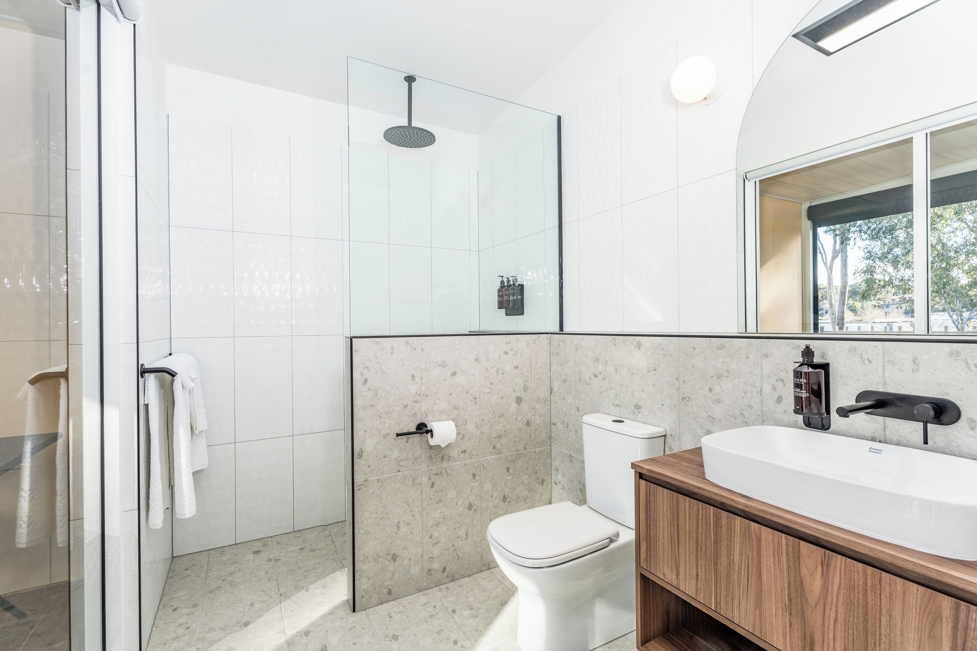 A modern bathroom with a glass shower enclosure, a toilet, and a wooden vanity with a sink.