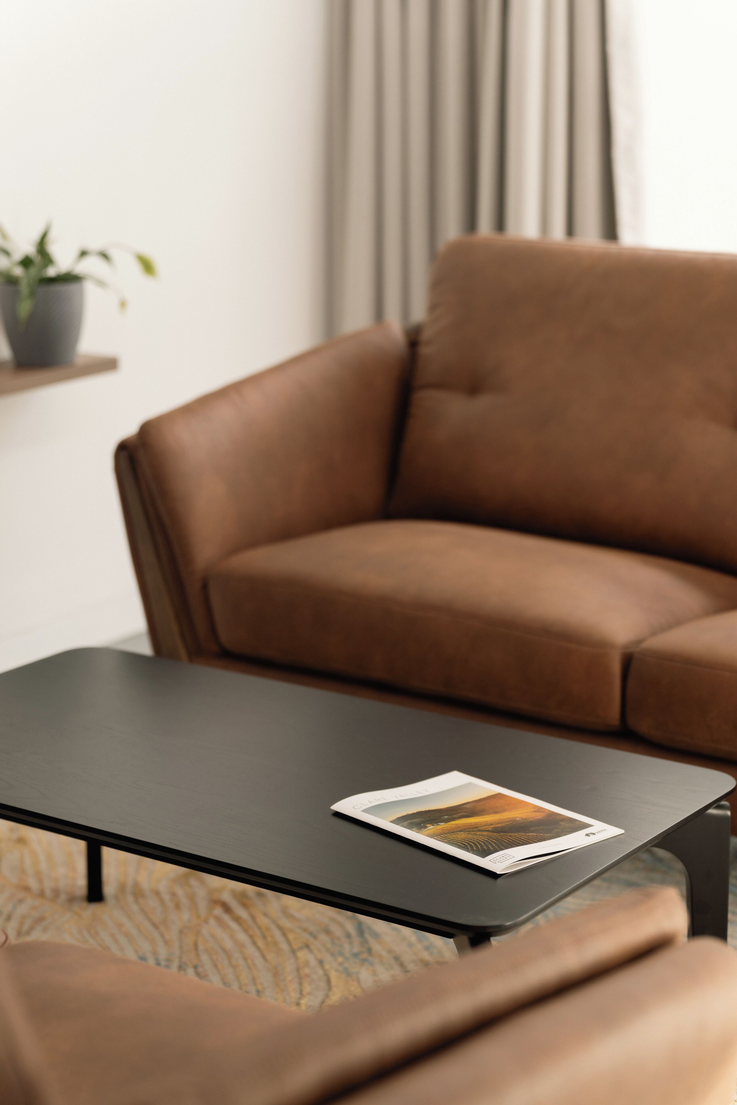 A brown leather sofa and a black coffee table with a magazine.