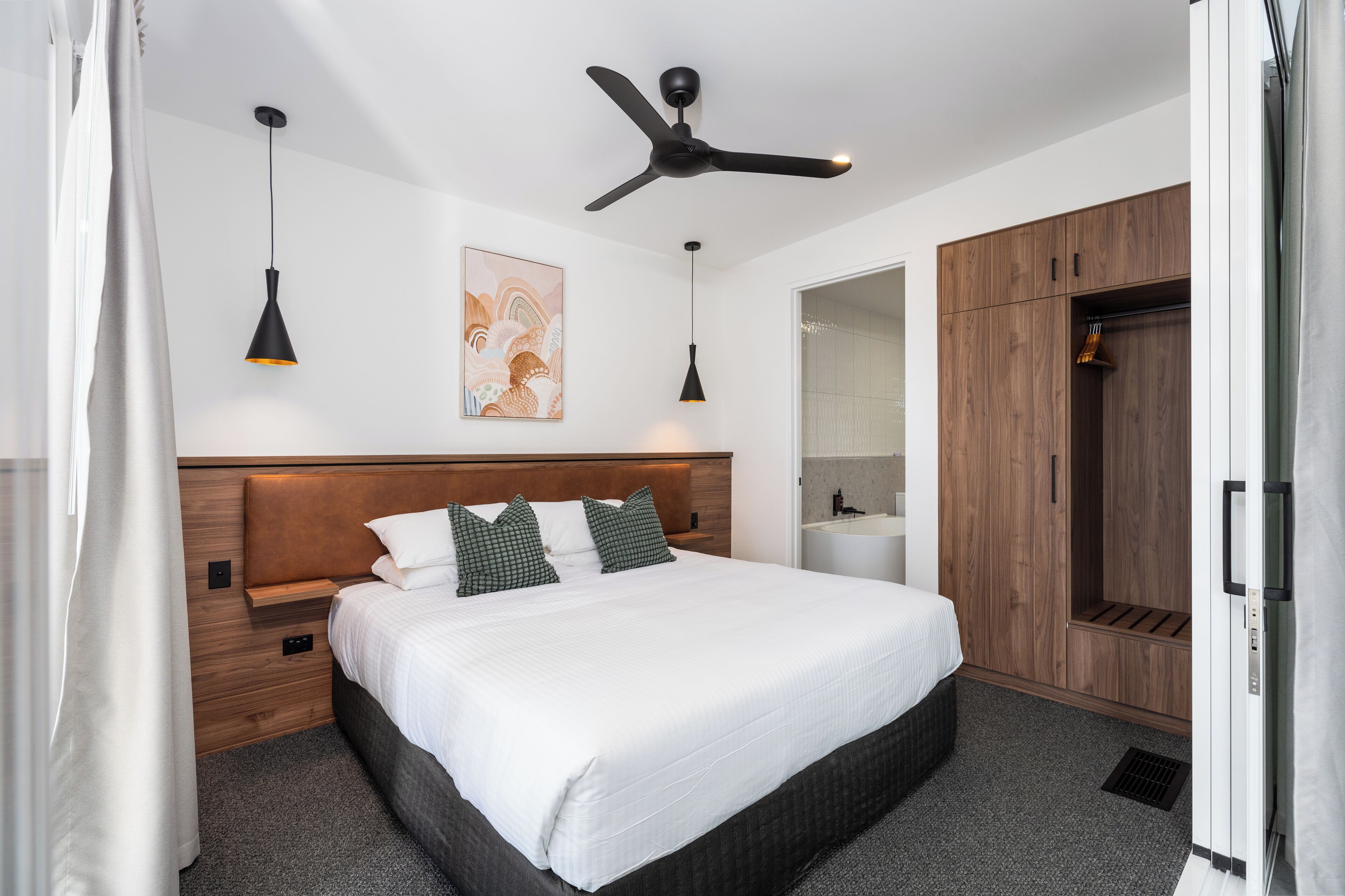 Un dormitorio moderno con una cama grande, cabecera de madera, ventilador de techo, lámparas colgantes y un armario.