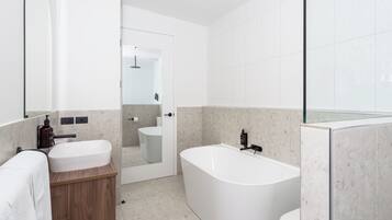 Ein modernes Badezimmer mit einer freistehenden Badewanne, einem Waschtisch mit Spiegel und einer Toilette.