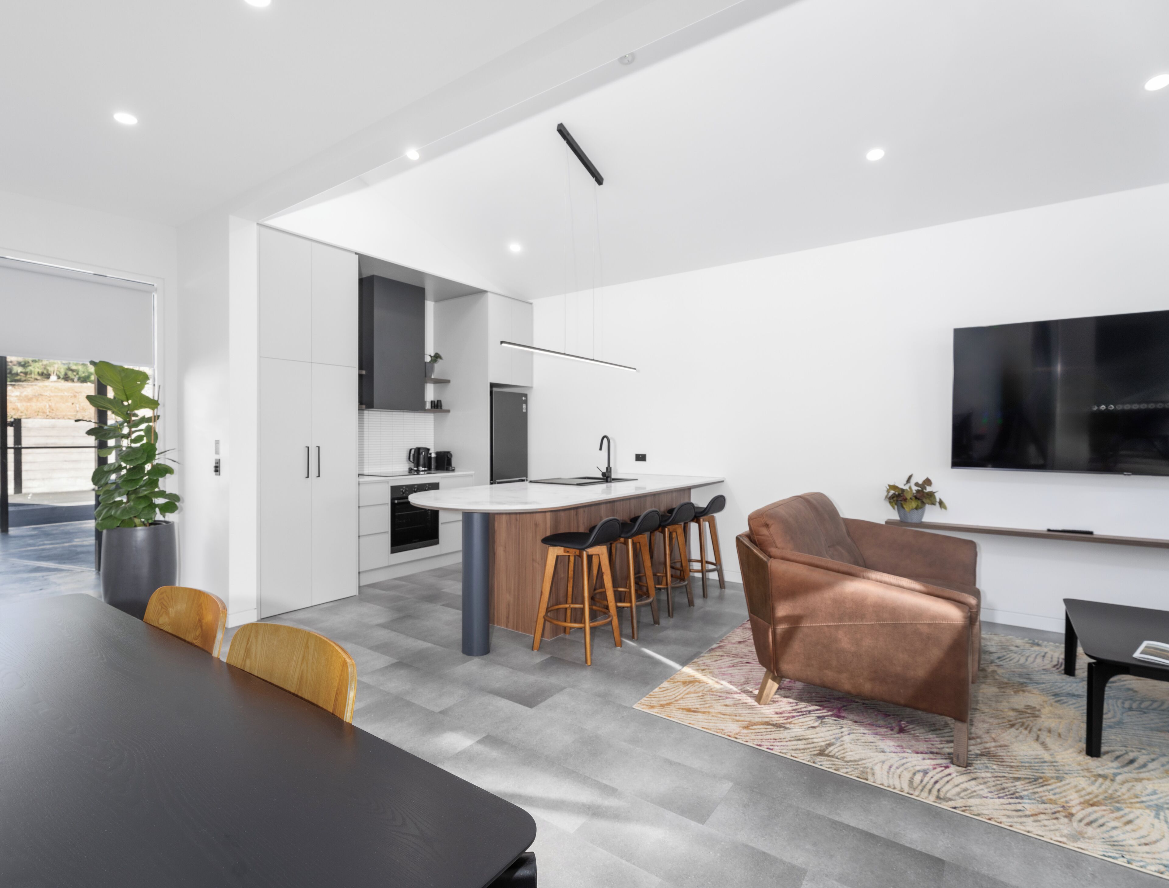 Una cocina moderna con una isla central, taburetes de bar, un sofá y un televisor montado en la pared.