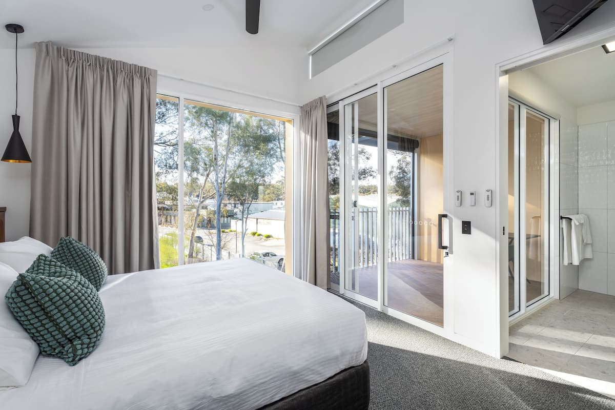 Ein modernes Hotelzimmer mit einem großen Bett, einer Schiebetür zum Balkon und Blick ins Freie.