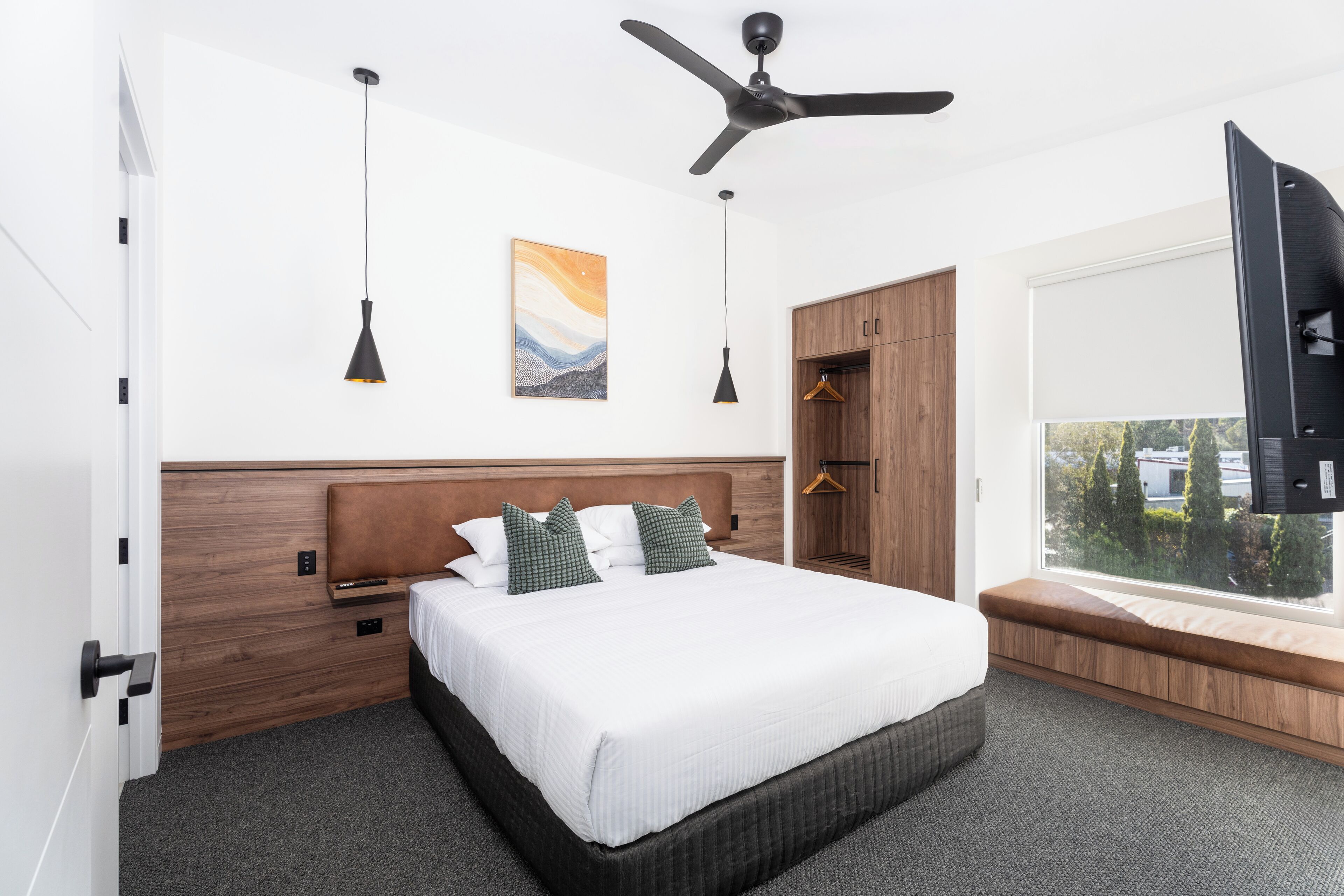 A modern hotel bedroom with a large bed, a ceiling fan, a window with a view, and a wardrobe.