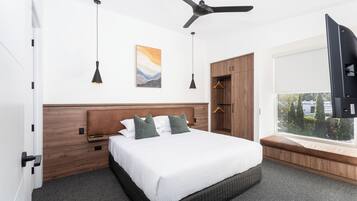 Un dormitorio de hotel moderno con una cama grande, un ventilador de techo, una ventana con vistas y un armario.