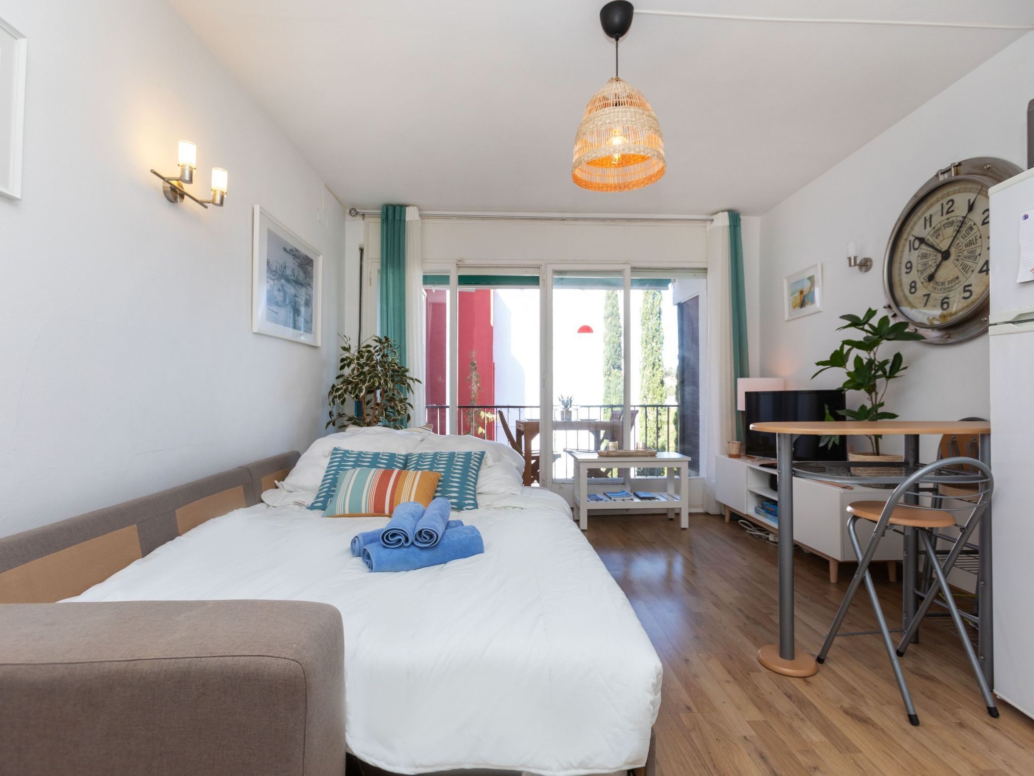 Un dormitorio con cama, escritorio, silla, lámpara colgante y un reloj en la pared.