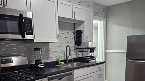 A modern kitchen with stainless steel appliances, white cabinetry, and a patterned rug. - Cozy 2BR Home in Delmar Loop (University City)