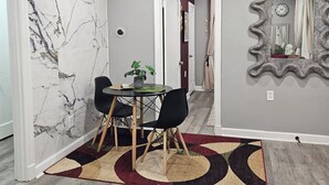 A dining area with a marble wall, a round table with chairs, a patterned rug, and a mirror on the wall. - Cozy 2BR Home in Delmar Loop (University City)