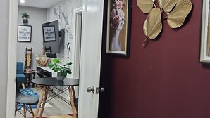 A hallway with a red wall, a white door, and a decorative gold leaf wall art. There is a framed picture on the wall and a potted plant on the floor. - Cozy 2BR Home in Delmar Loop (University City)