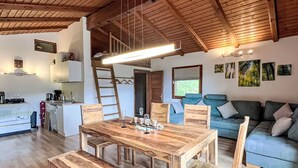 Ein gemütliches, rustikales Blockhäuschen mit Holztisch, Bänken, einer Couch und einer kleinen Küche.