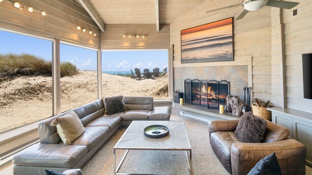 Un salón amplio con una ventana grande que da a una playa, una chimenea y muebles de cuero.