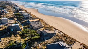 Una zona residencial costera con casas a lo largo de la playa, una vista despejada del océano y un horizonte urbano lejano.