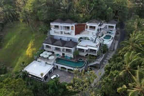 Un resort de varios pisos con piscina, varios balcones y vegetación exuberante que lo rodea.
