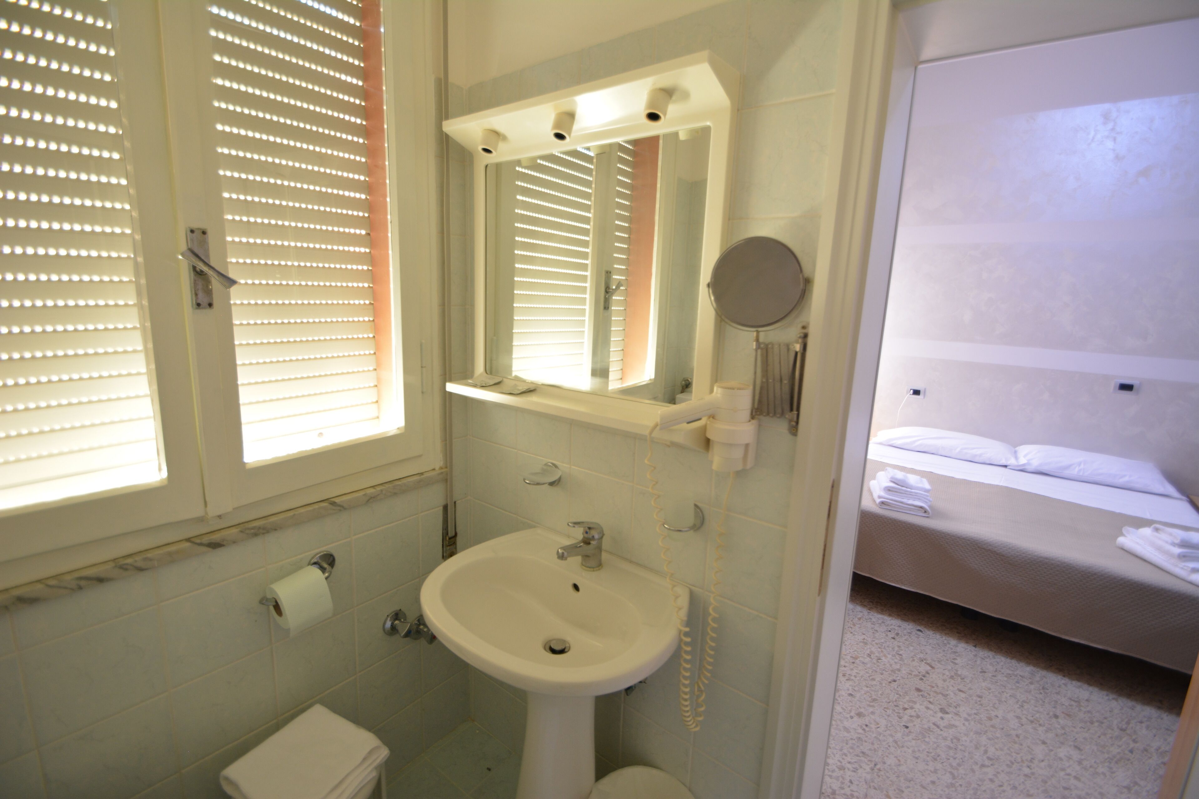 A bathroom with a sink, toilet, and window with blinds.