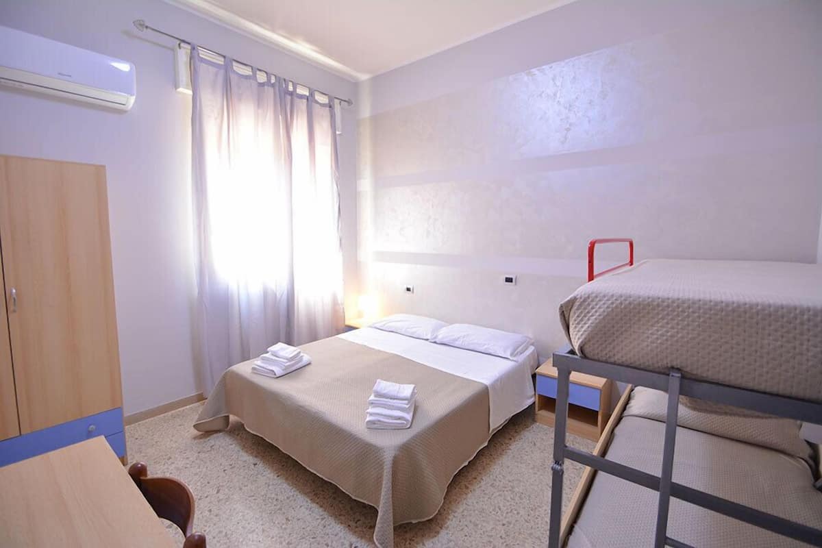 A room with two beds, a wooden wardrobe, a small table, and a window with curtains.
