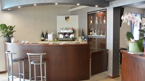 A bar area with a counter, stools, a coffee machine, and a wine bottle. - Hotel  Bella  Romagna  (Ravenna)