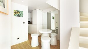 Een moderne, minimalistisch ingerichte kamer met een houten vloer, witte muren en een ronde centrale tafel met krukjes.