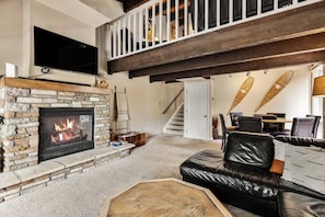 A living room with a stone fireplace, a black leather sofa, and a staircase leading to an upper level.