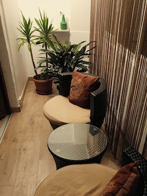 Een hoekzaal met een stoel, een tafeltje, twee potplanten en een gordijn.