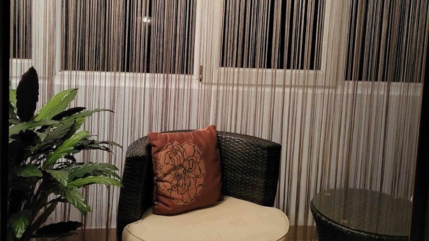 Una habitación con una silla de mimbre, una mesa de vidrio y una planta en maceta.