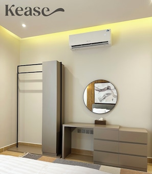 A modern hotel room with a bed, a wardrobe, a vanity with a mirror, and an air conditioning unit.