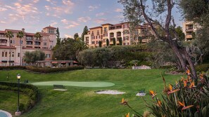 Un parcours de golf avec un green d’entraînement, un espace patio doté de sièges en plein air, et un grand bâtiment avec de nombreux balcons en arrière-plan.