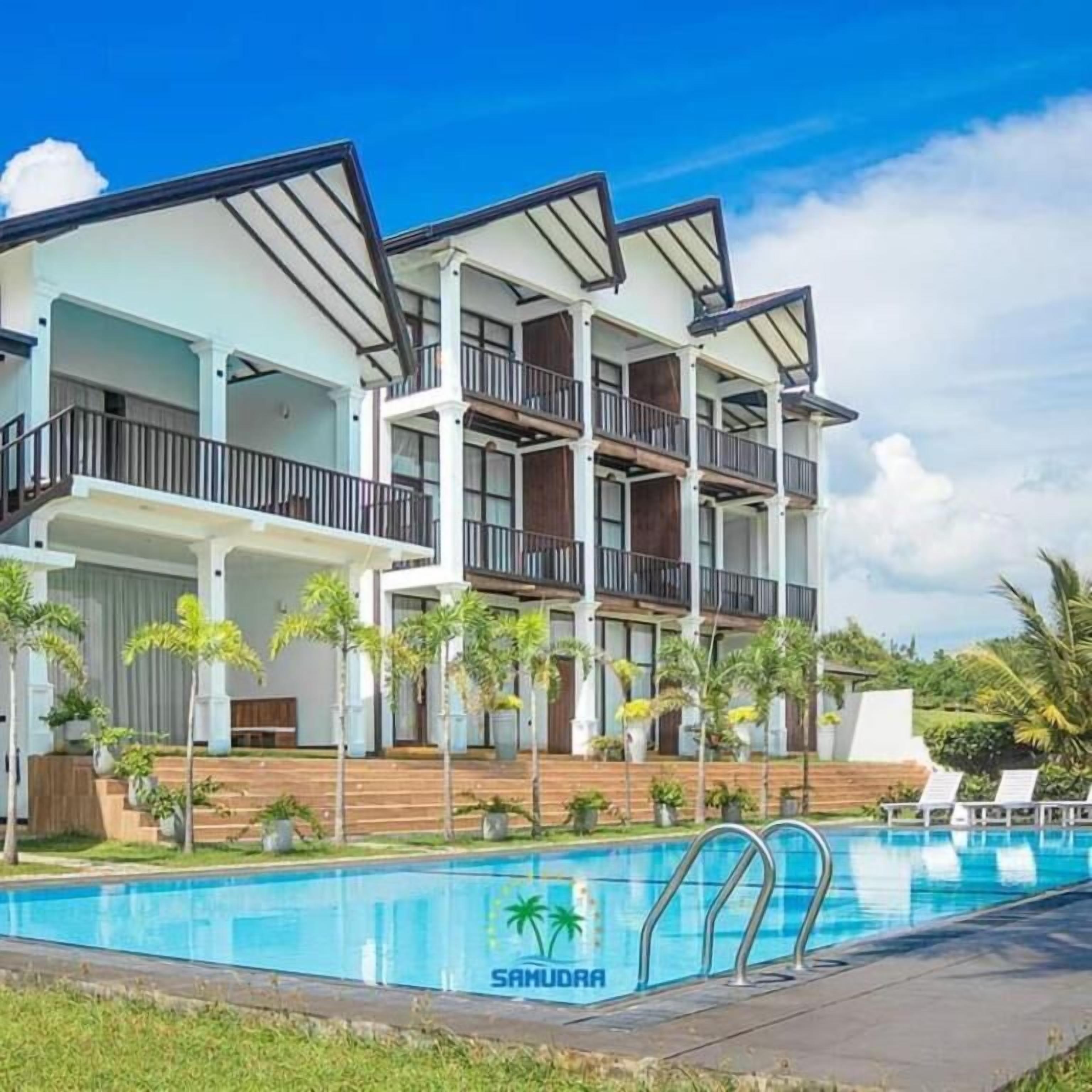 A multi-story hotel with a pool area, featuring balconies and a tropical garden.