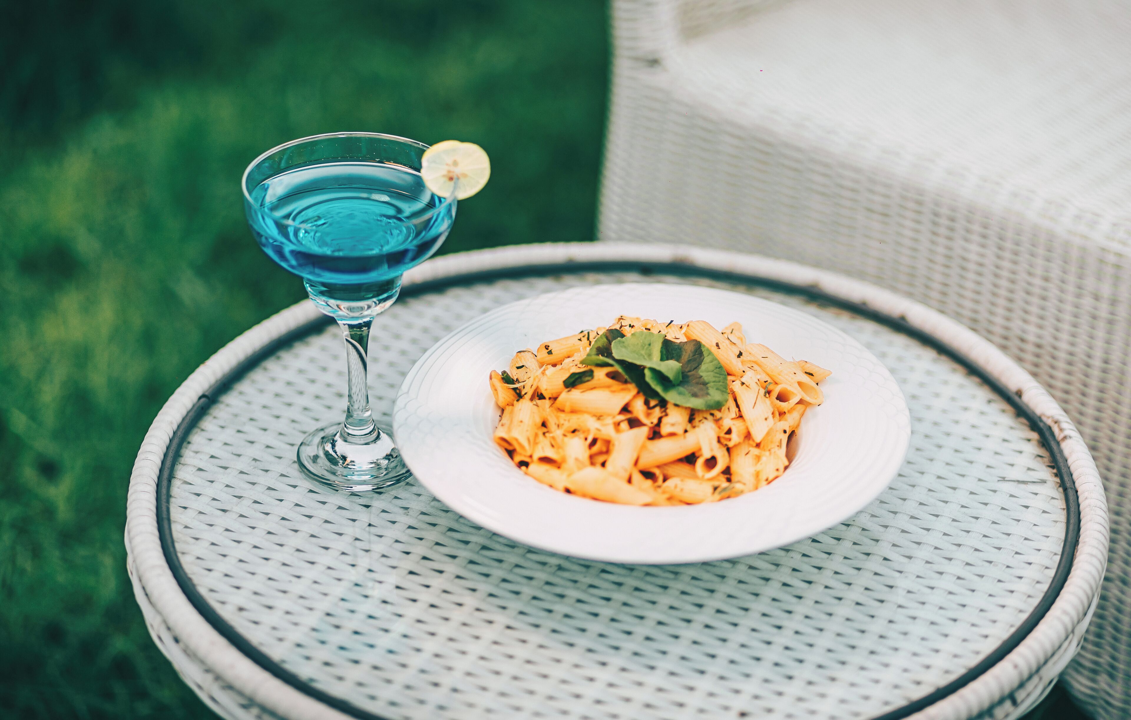 A plate of pasta with a lemon garnish on a round table with a textured surface.