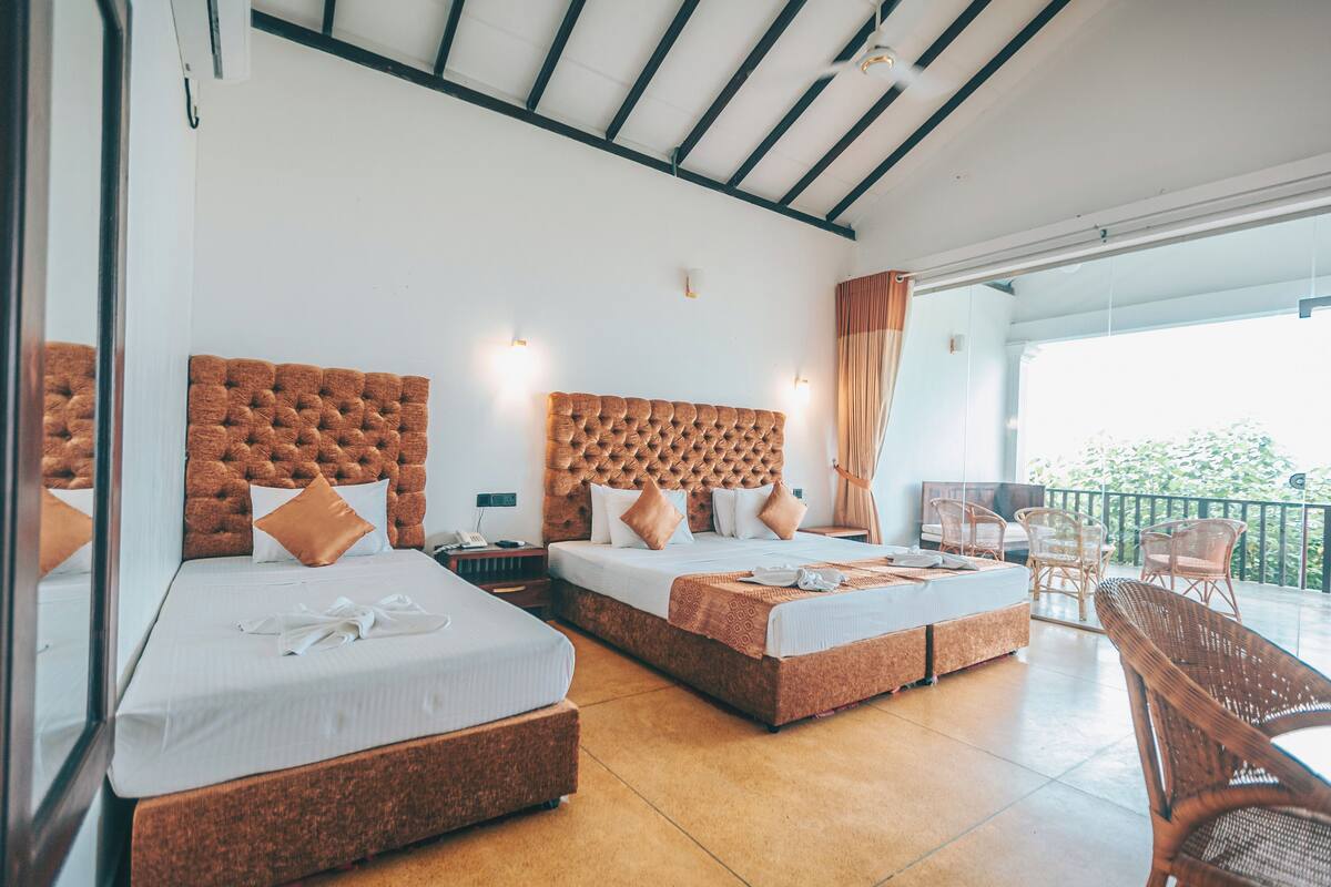 A hotel room with two beds, a balcony with wicker chairs, and a large window.