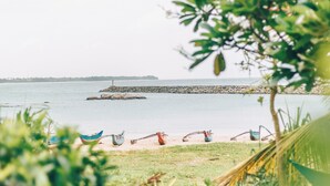 A beach view with boats, a rocky breakwater, and lush greenery. - Samudra Beach Resort (Rekawa)